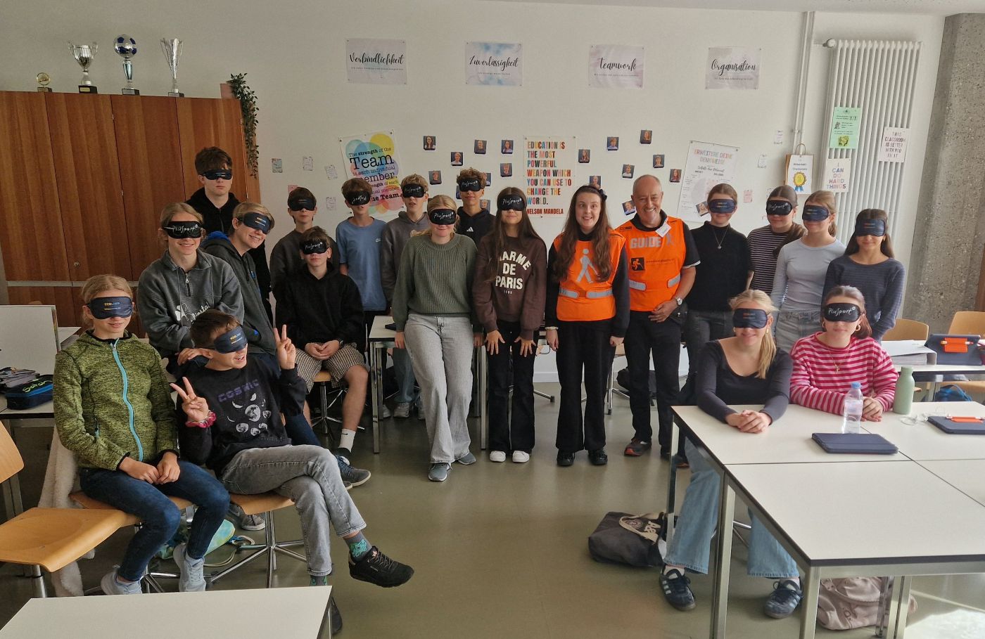 Sensibilisierungsworkshop an einer Sekundarschule in Liestal: Klassenfoto mit den Lehrpersonen, Läuferin Salomé und Guide Gabor im Klassenzimmer mit Dunkelbrillen aufgesetzt