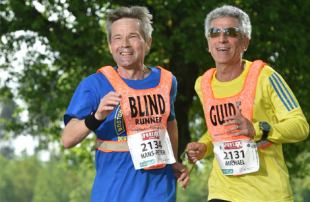 Ein Blindenguide und ein Blindjogger, die an einem Laufsport-Event teilnehmen.