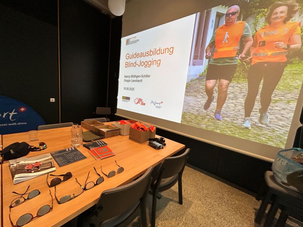 Blind-Jogging Präsentation im Rahmen der Guideausbildung: Titelfolie und ausgelegte Dunkelbrillen auf dem Tisch