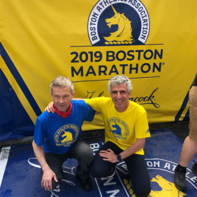 Hans-Peter und Mike knieen vor einer Flagge des 2019 Boston Marathons.